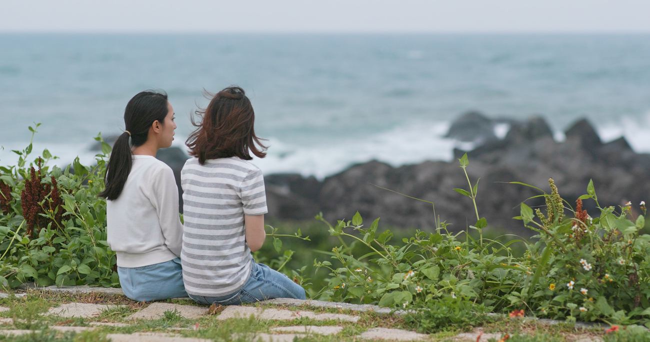 Two friends sitting together by the ocean, talking